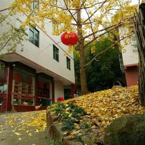 A building with a red lantern, a tree with yellow leaves, and a pile of fallen leaves. - Wang Xing Hotel (Nanxiong)