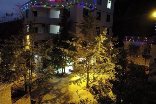 A multi-story building with balconies, surrounded by trees and illuminated by string lights.