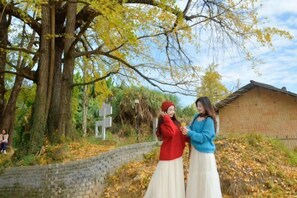 Two individuals standing in a natural setting with a brick building and a stone wall in the background. - Wang Xing Hotel (Nanxiong)