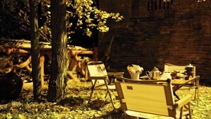 A rustic outdoor seating area with wooden chairs and a table, surrounded by trees and a brick wall. - Wang Xing Hotel (Nanxiong)