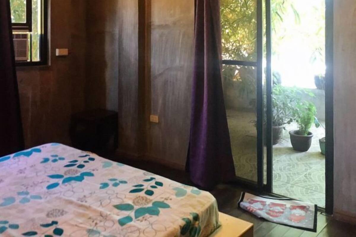 A room with a bed, a window, and a sliding door leading to an outdoor area with potted plants.