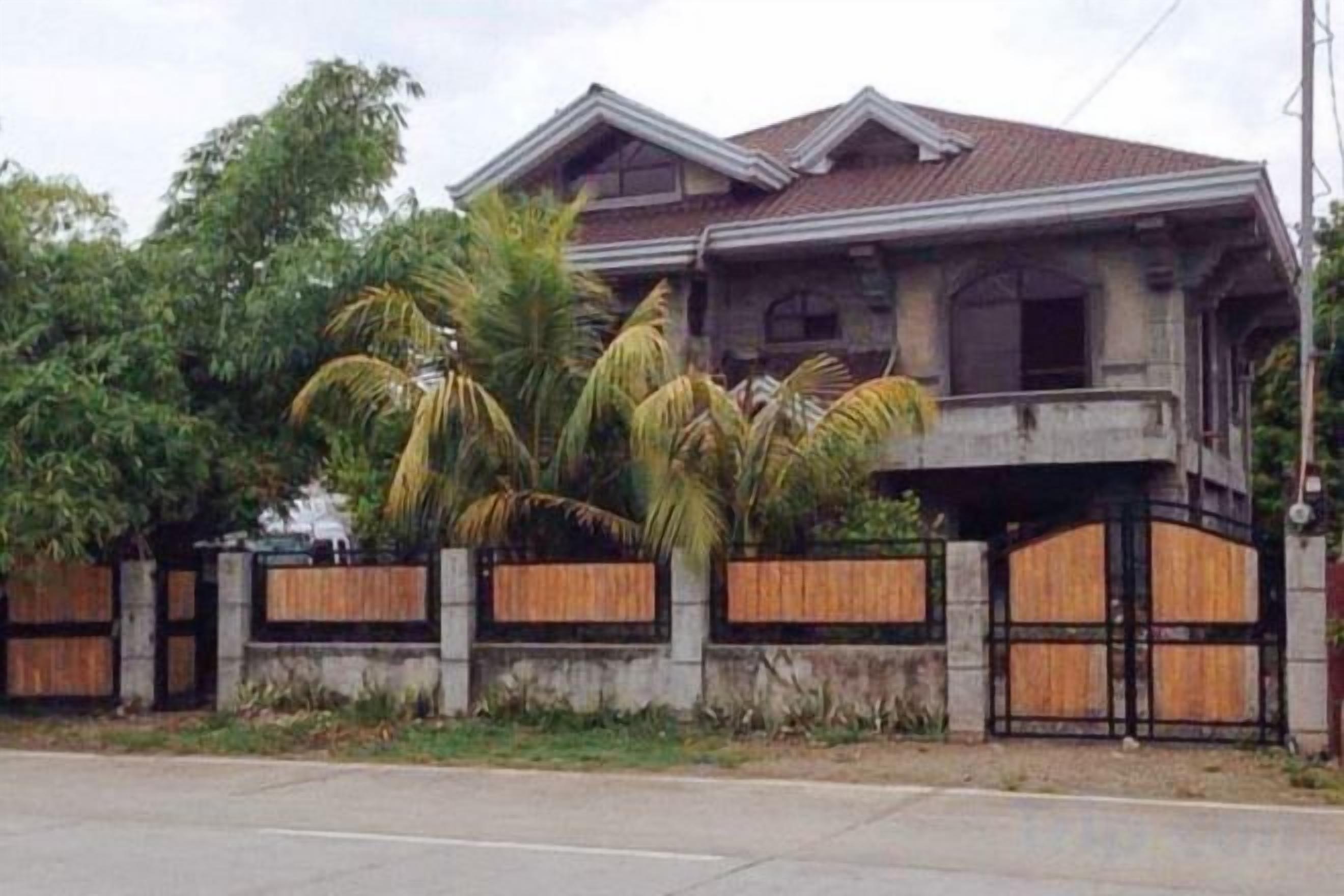 Una casa de dos pisos con balcón, rodeada por una valla de madera y palmeras.