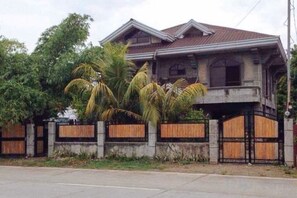 A two-story house with a balcony, surrounded by a wooden fence and palm trees. - RedDoorz Hostel @ Madrias Pension House Isabela (Delfin Albano)