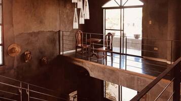A high-ceilinged room with a staircase, a dining area, and a large arched window.