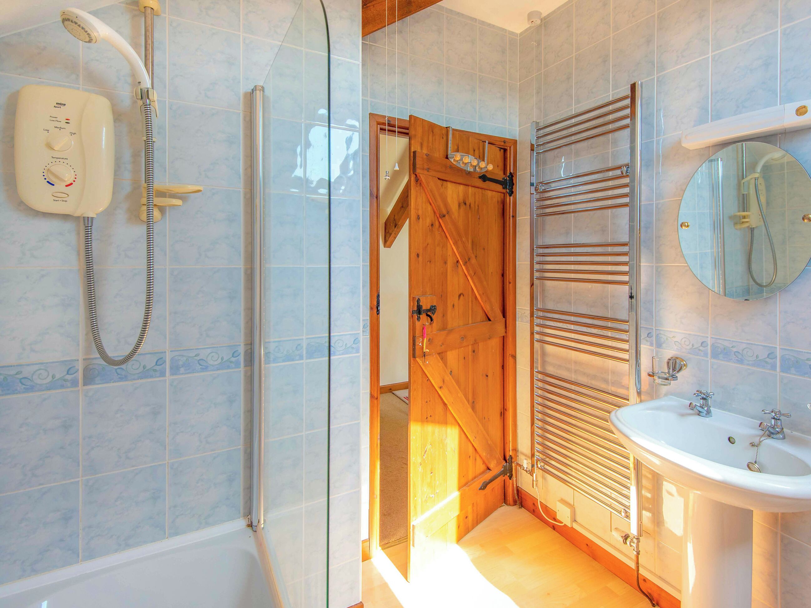 A bathroom with a shower, a wooden door, a towel rack, and a sink.