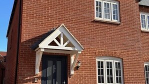 A red brick house with a dark front door, white-framed windows, and a small porch area.
