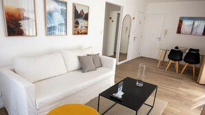 Un salon moderne avec un canapé blanc, un fauteuil jaune, une table basse noire et un coin repas avec deux chaises.