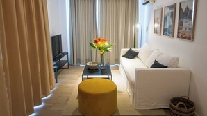 Un salon moderne avec un canapé, une table basse, un téléviseur et un pouf jaune.