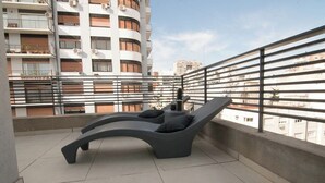 Un espace de détente extérieur moderne, avec un fauteuil incurvé et une petite table, le tout entouré d’une rambarde en métal.