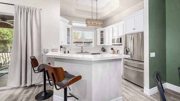 A modern kitchen with white cabinetry, a central island, stainless steel appliances, and a dining area with bar stools. - New Property TPC Golf Course | 4 Beds | Golf Dream (Scottsdale)