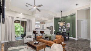 A spacious living room with a sofa, coffee table, and ottoman, a dining area with a chandelier, and a kitchen with white cabinets. - New Property TPC Golf Course | 4 Beds | Golf Dream (Scottsdale)