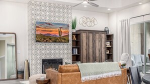 A living room with a brown leather sofa, a fireplace, a bookshelf, and a large window with curtains. - New Property TPC Golf Course | 4 Beds | Golf Dream (Scottsdale)