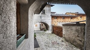 A courtyard with stone walls, a wooden fence, and a building with a sloped roof. - Sesto Senso - Three Bedroom Apartment, Sleeps 8 (Ponte di legno)