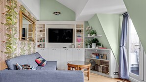 Una sala de estar moderna con un sofá gris, una mesa redonda de madera y un televisor montado en un mueble blanco.