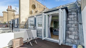 Terraza en la azotea con una bañera blanca, un taburete de madera y una silla.