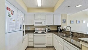 A small kitchen with white cabinets, a stove, a microwave, a sink, and a refrigerator. - Carolinian 1732-Oceanfront 2BR/2BA-Pool (Myrtle Beach)