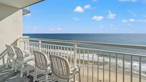 A balcony with white chairs overlooking a beach with waves. - Carolinian 1732-Oceanfront 2BR/2BA-Pool (Myrtle Beach)