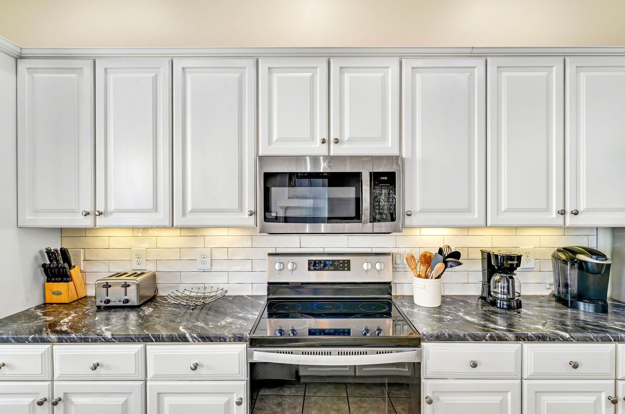 A kitchen with white cabinets, a stainless steel microwave, a toaster, and a coffee maker.