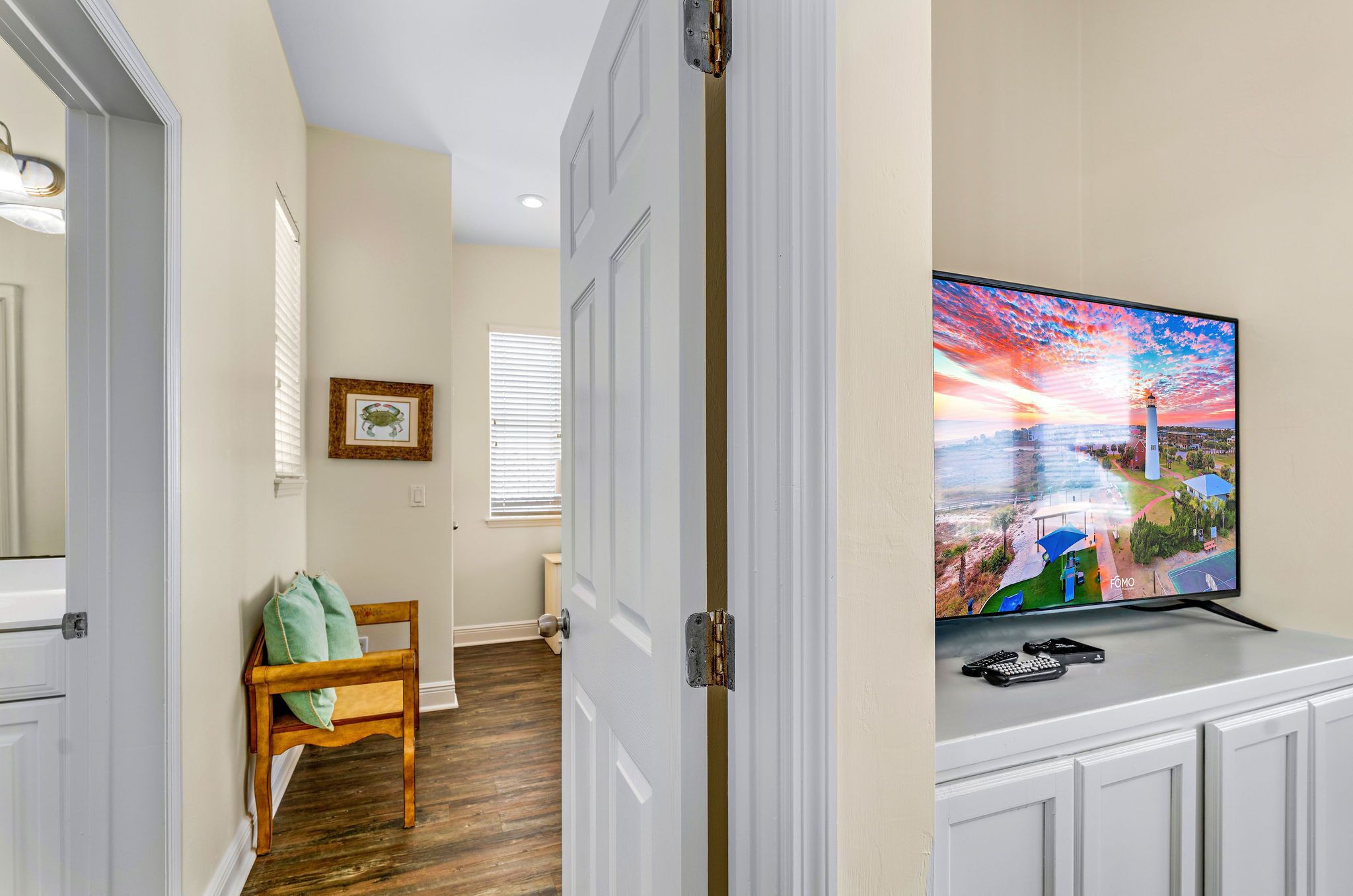 A hallway with a wooden chair, a framed picture on the wall, and a television displaying a sunset scene.