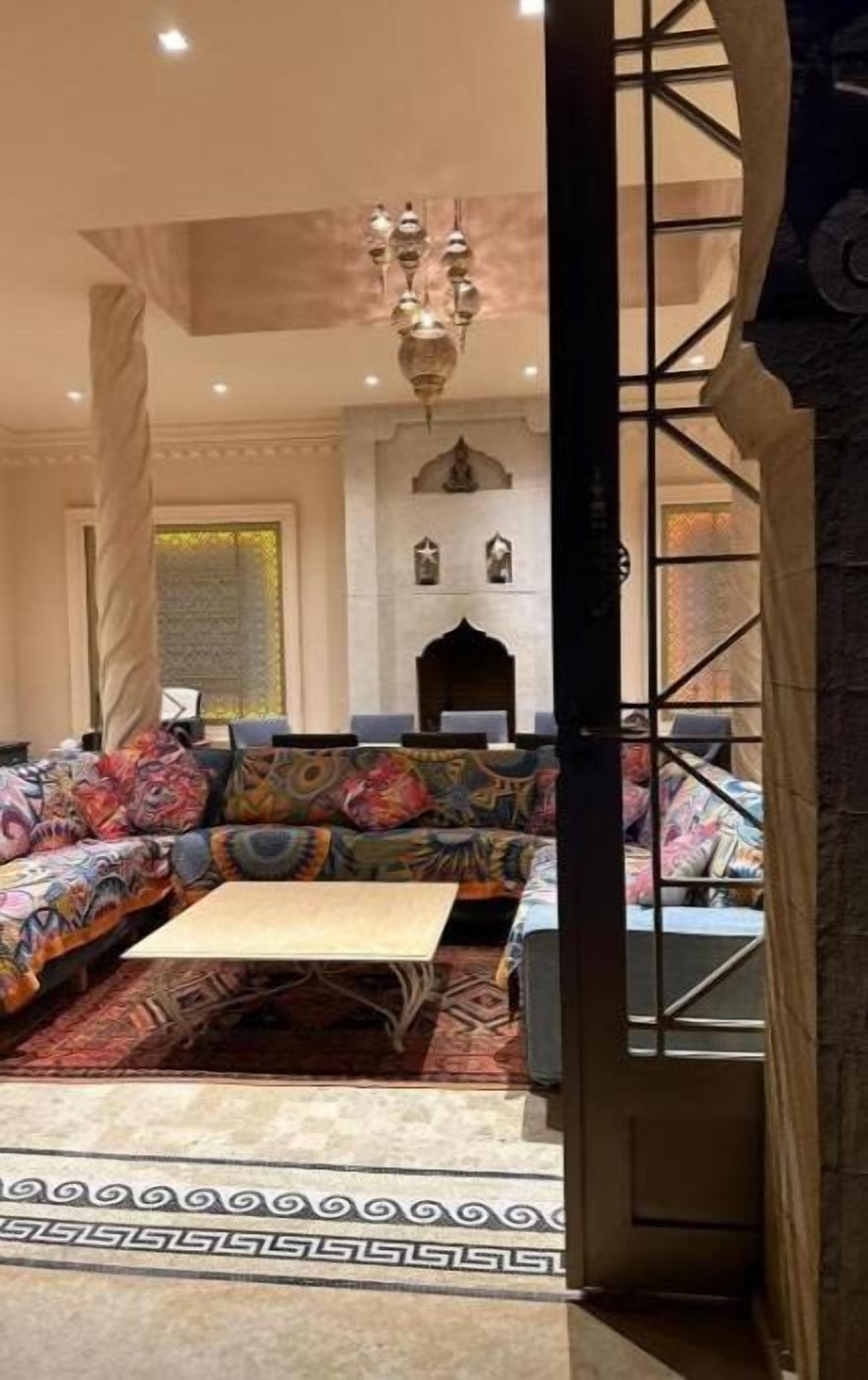 Ein Zimmer mit einem farbenfrohen Sofa, einem kleinen Tisch und einem gemusterten Teppich. An der Wand befindet sich eine Dekoration mit einer Statue und einer Chandeliebre.