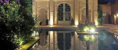 A traditional building with arched doorways and a pool in front.