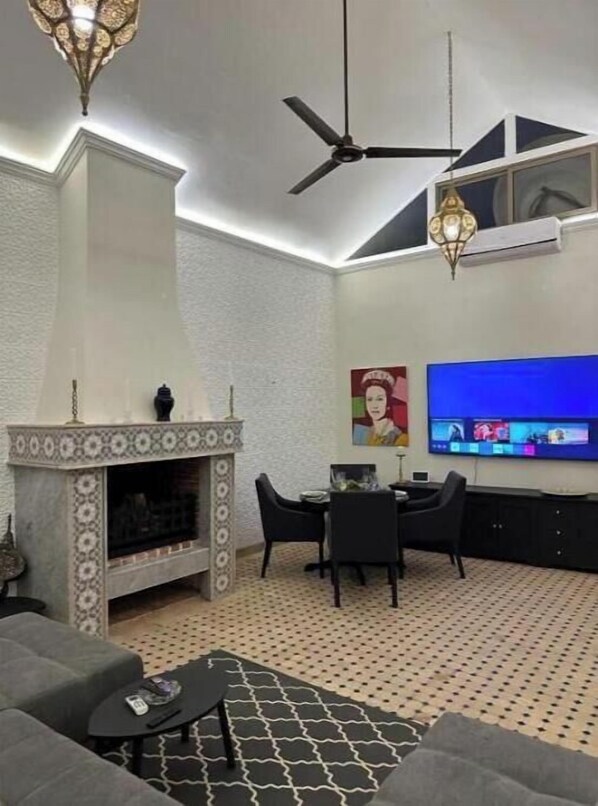 Un salon doté d’une cheminée, d’un ventilateur de plafond, d’un téléviseur fixé au mur et d’un sol à motifs.