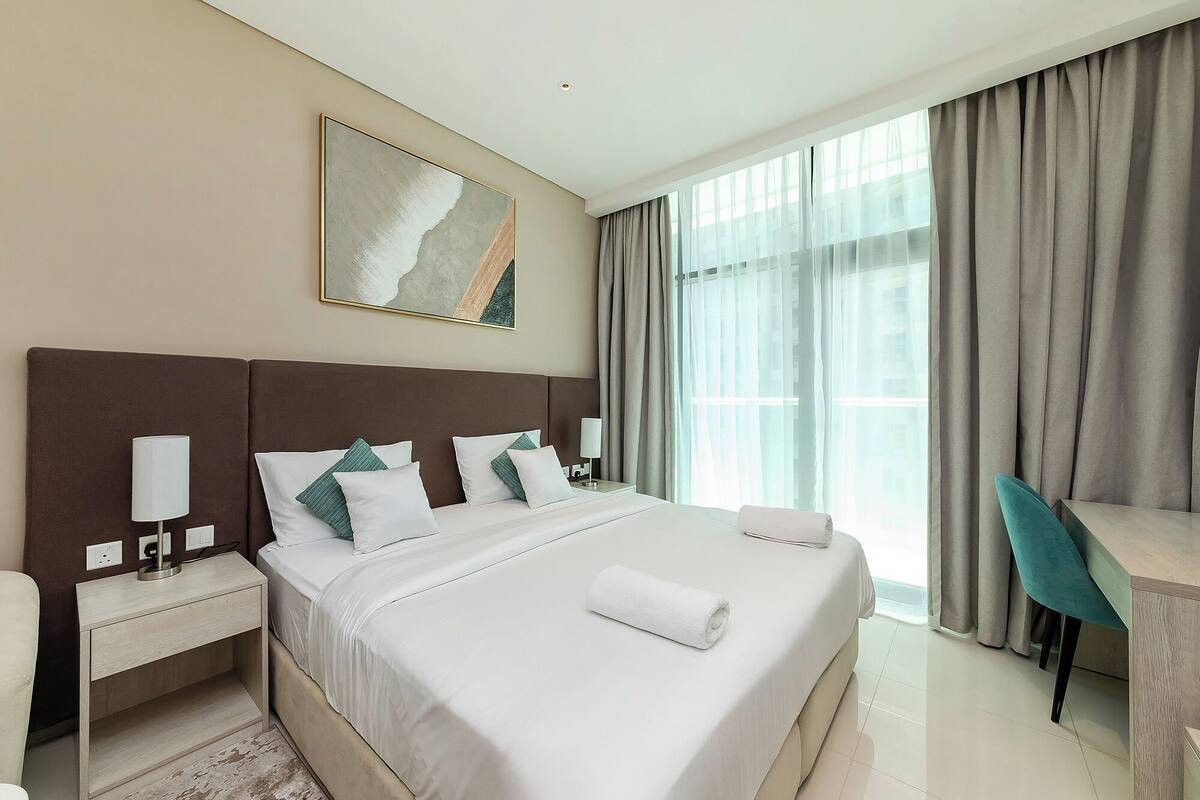 A hotel room with a large bed, a desk, and a window with curtains.