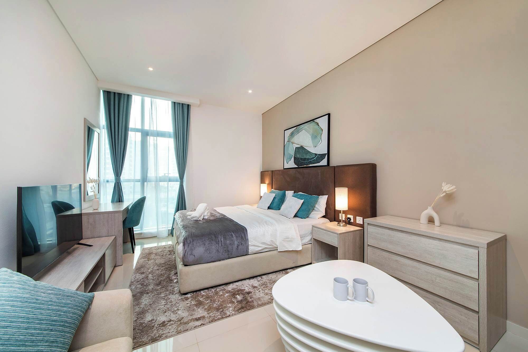 Una habitación de hotel moderna con cama, mesitas de noche, un escritorio y una mesa de centro redonda.
