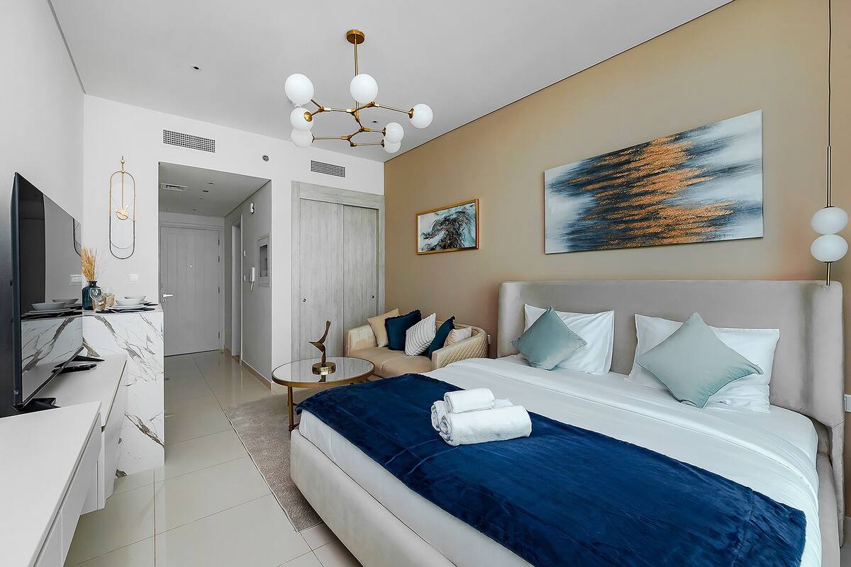 A modern hotel room with a large bed, a sitting area, and a view of the hallway.