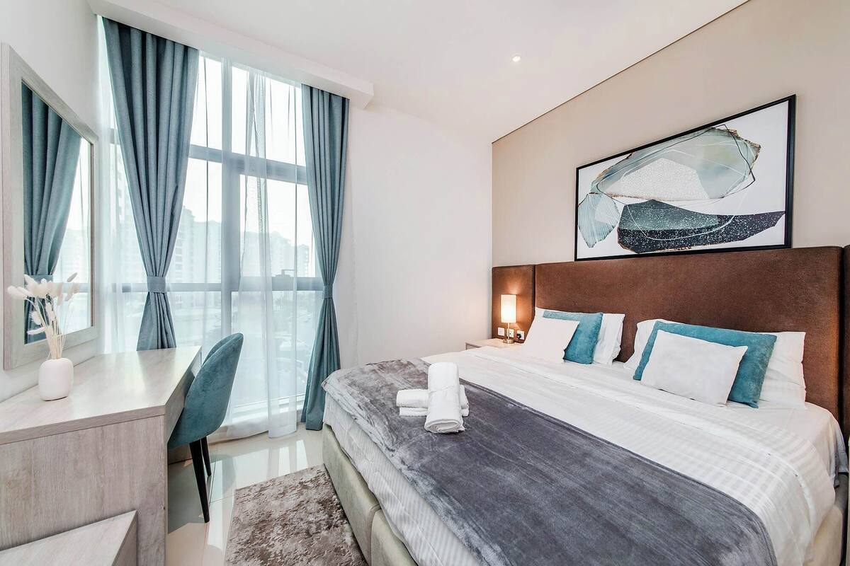 A modern hotel room with a large bed, a desk, and a window with curtains.
