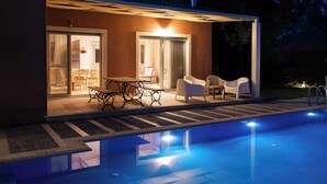 Un espace piscine extérieur moderne, doté d’une table et de chaises pour les repas, d’un coin salon abrité et offrant une vue sur la piscine.