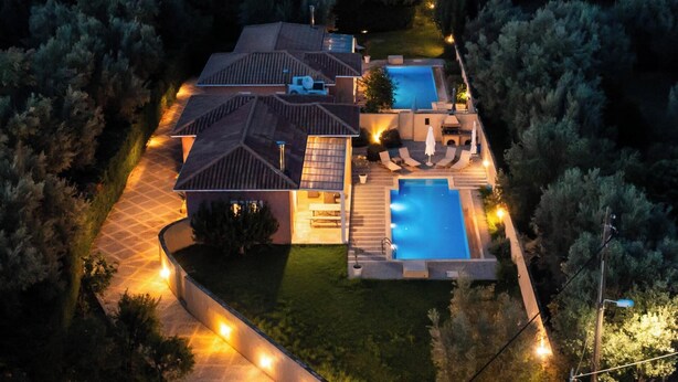 Une grande maison avec une piscine, un patio couvert et une allée bien éclairée.