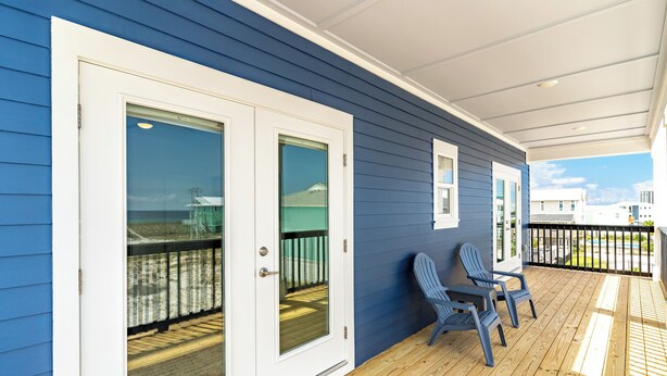 A covered porch with blue siding, two glass doors, and two Adirondack chairs. - Spacious new build 6-bedroom 6.5 bath house in gorgeous Navarre Beach (Navarre)