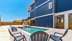 A pool area with a blue building, outdoor seating, and a wooden fence. - Spacious new build 6-bedroom 6.5 bath house in gorgeous Navarre Beach (Navarre)