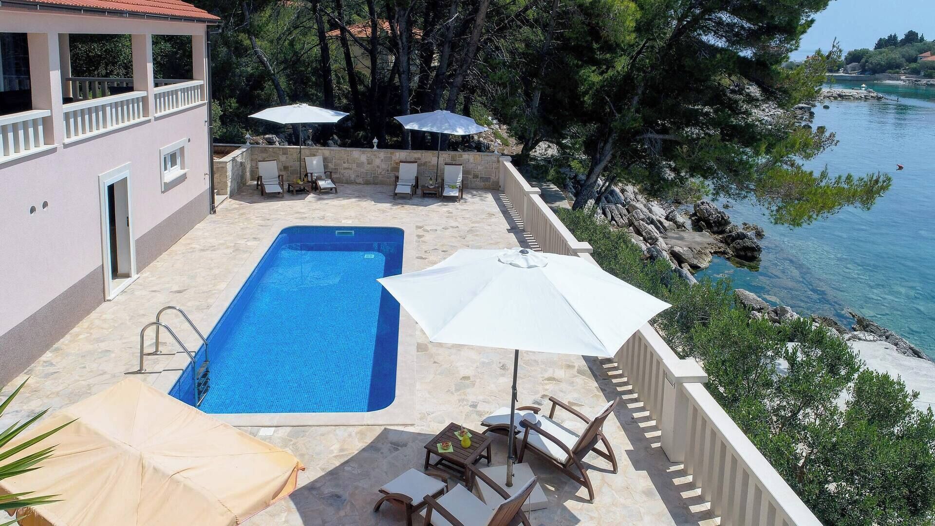 A swimming pool with lounge chairs and umbrellas, surrounded by a stone deck and overlooking a body of water.