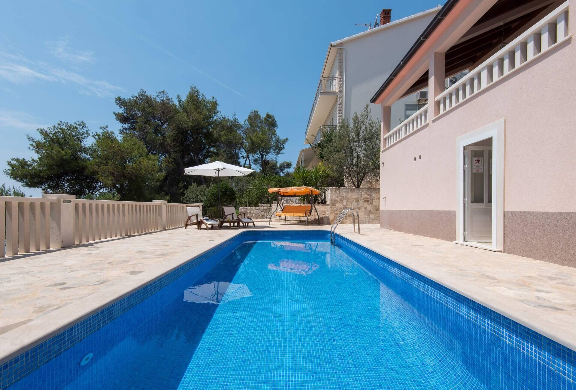 A swimming pool with lounge chairs and umbrellas, surrounded by a stone wall and trees.