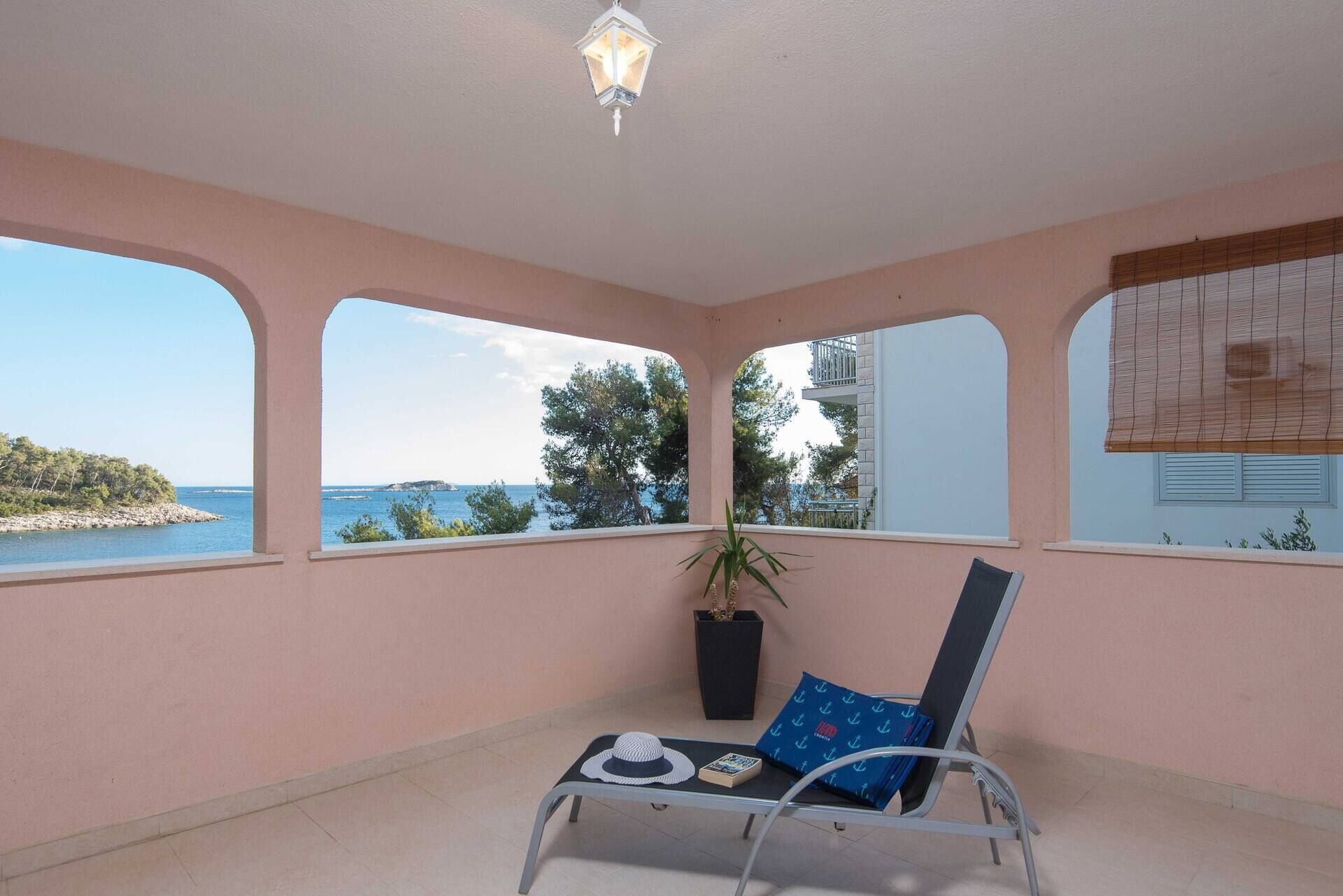 A balcony with a view of the sea, a potted plant, and a lounge chair with a cushion.