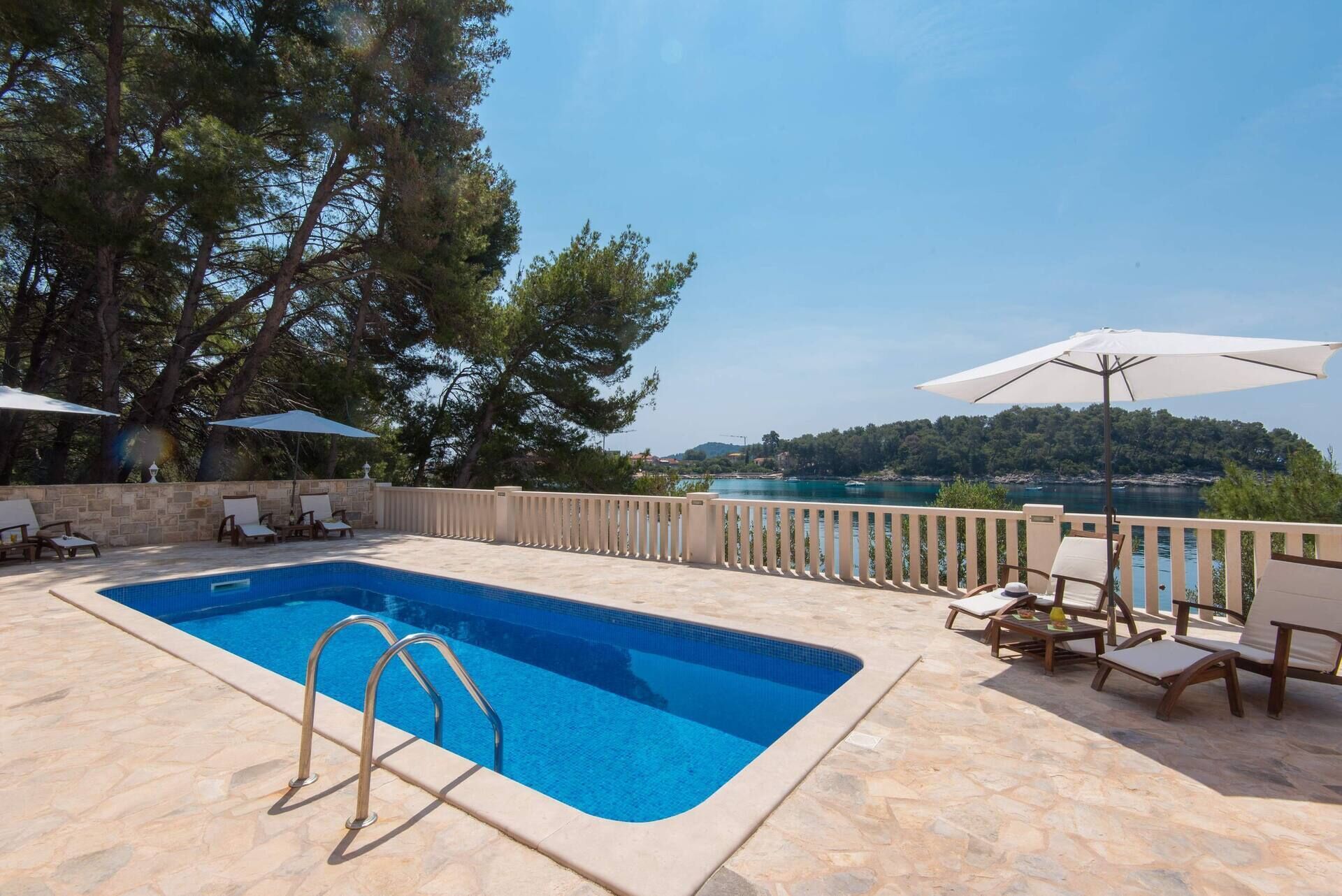 A swimming pool with a stone deck, lounge chairs, and umbrellas.