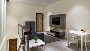 Un salon moderne avec un canapé, un téléviseur fixé au mur, une table à manger et un escalier.