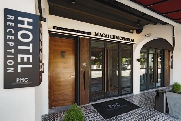 Entrada de hotel com balcão de recepção, placa indicativa e porta com a inscrição 'Atendimento à Recepção'.