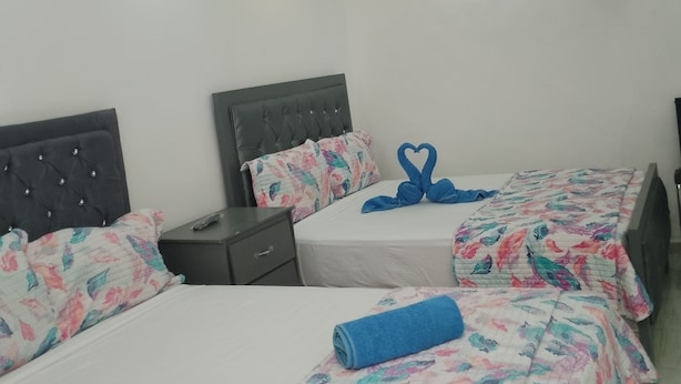 Een hotelkamer met twee bedden, elk voorzien van beddengoed met bloemenprint en handdoekjes in de vorm van een hart. Er zijn nachtkastjes met afstandsbedieningen en een airconditioner die aan de muur is bevestigd.