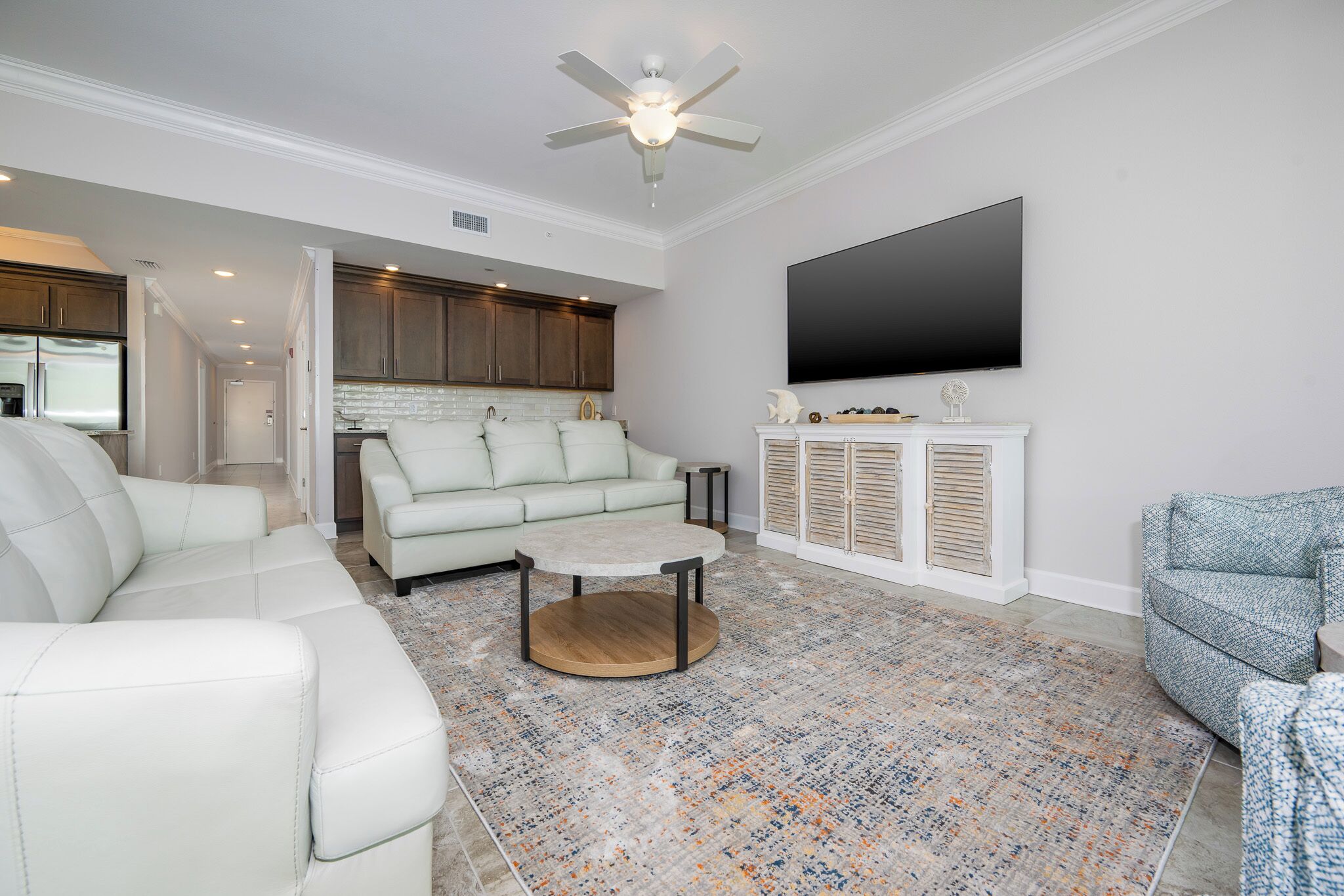 A modern living room with a sectional sofa, a coffee table, and a flat-screen TV mounted on the wall.