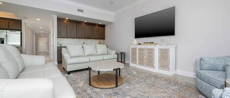 A modern living room with a sectional sofa, a coffee table, and a flat-screen TV mounted on the wall.