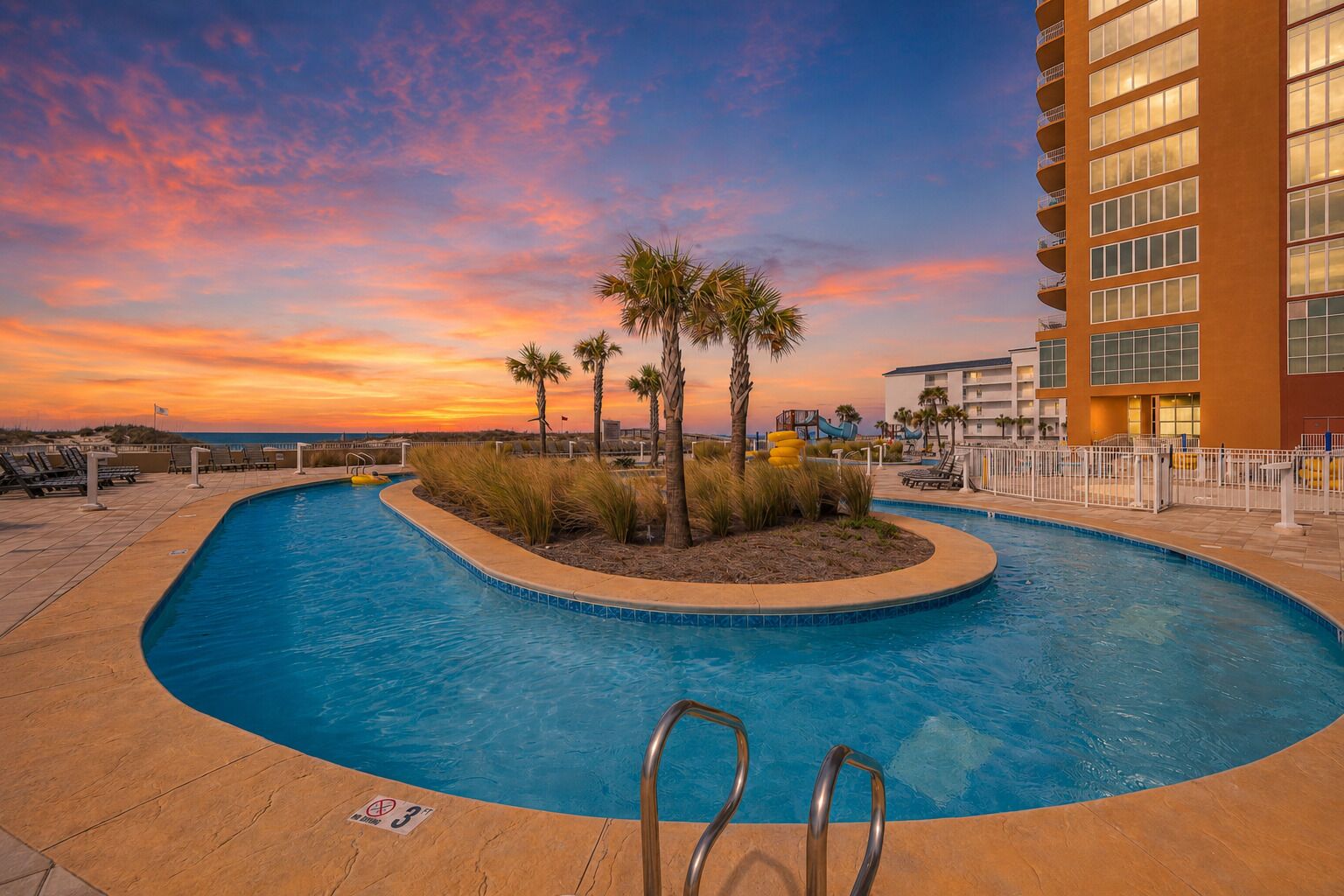 A swimming pool with a sunset view, palm trees, and a hotel building.
