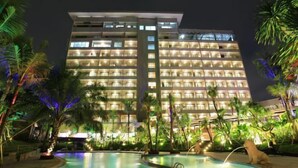 A multi-story hotel with a pool area, surrounded by palm trees and illuminated by artificial lighting. - Ijen Suites Resort & Convention (Klojen)