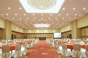 A large conference room with rows of tables and chairs, a stage with a screen, and a ceiling with recessed lighting. - Ijen Suites Resort & Convention (Klojen)