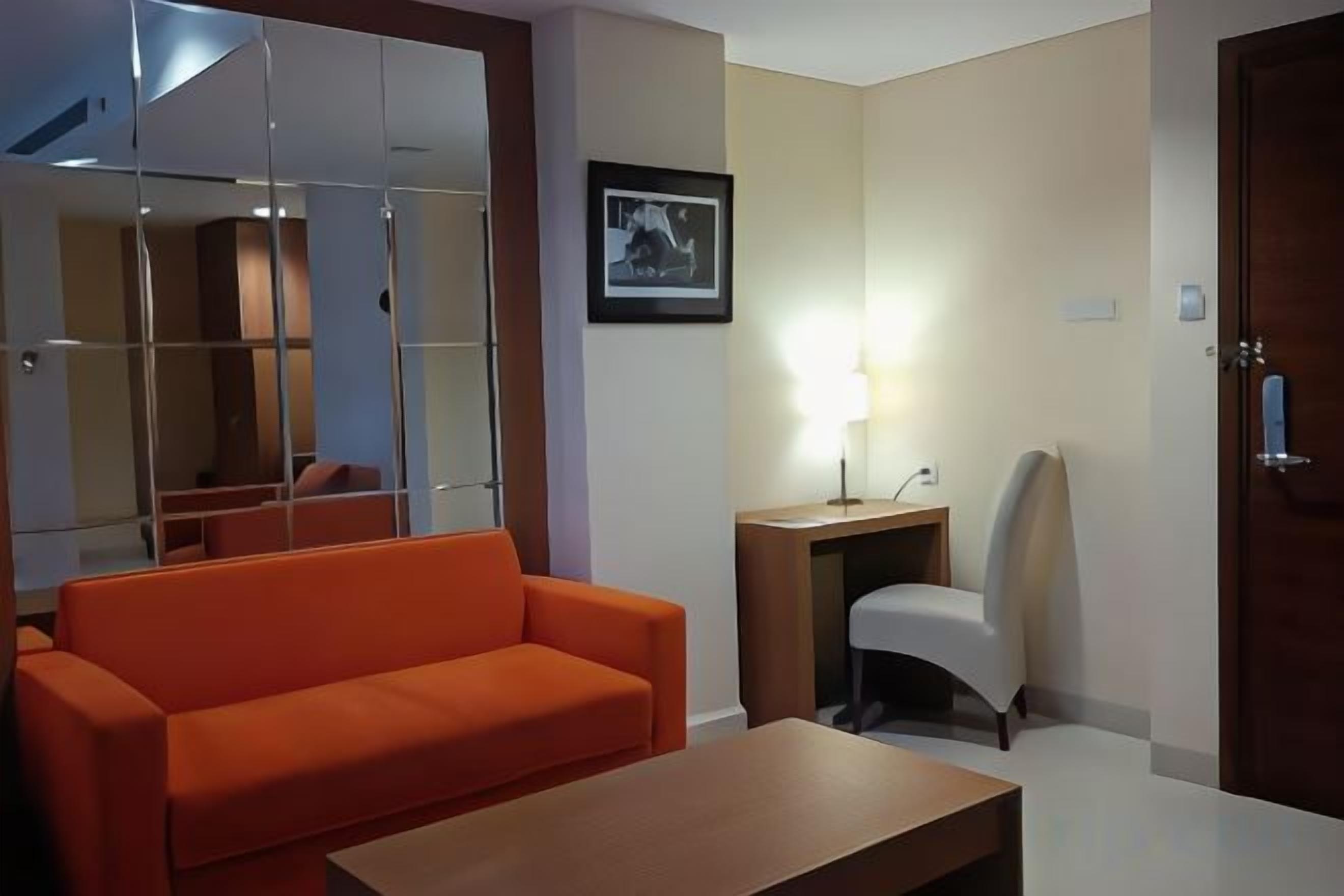 A room with a sofa, a desk, a chair, a mirror, and a door.