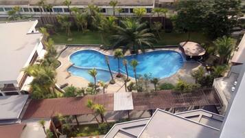 A swimming pool surrounded by palm trees and a building with a tiled roof.