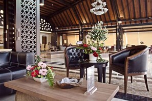 A lobby with a wooden ceiling, black leather sofas, a reception desk with a vase of flowers, and a large chandelier.