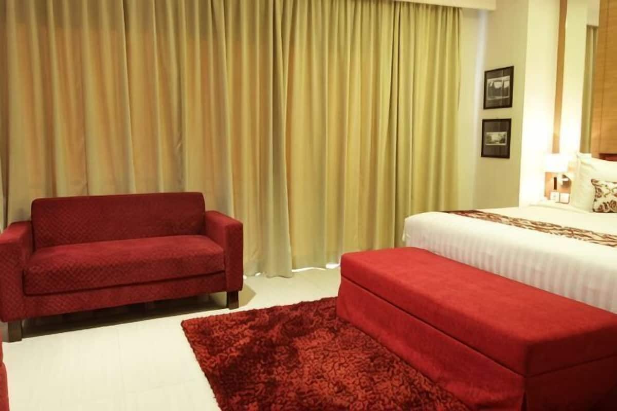 Ein Hotelzimmer mit einem Bett, einer roten Couch, einem roten Teppich und einem Vorhang.